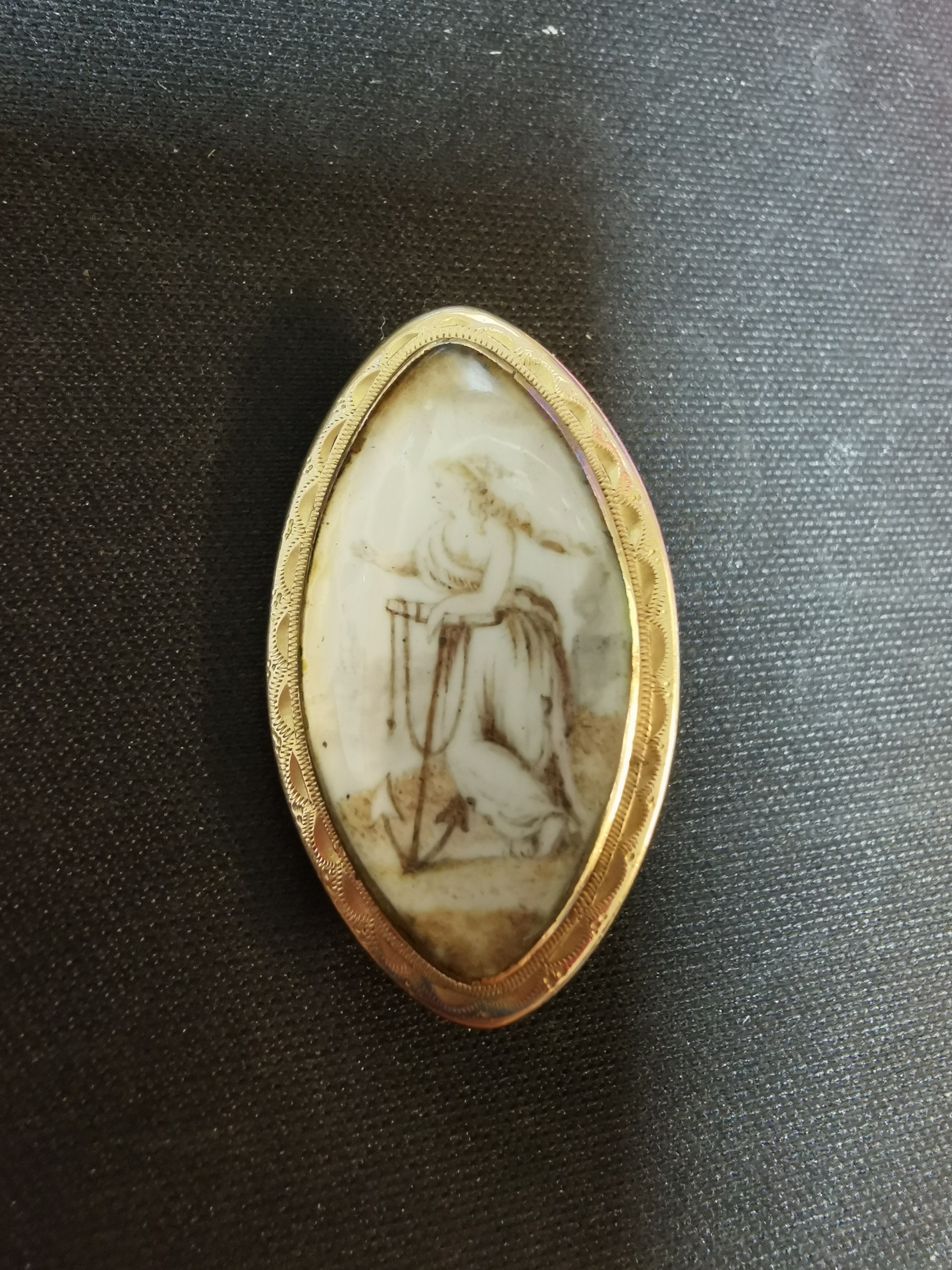 A Georgian yellow metal mourning brooch of oval form decorated with a lady leaning on an anchor on a