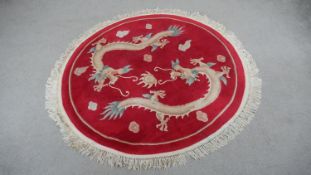 A Chinese rug with chasing dragons on a burgundy ground. D.158cm