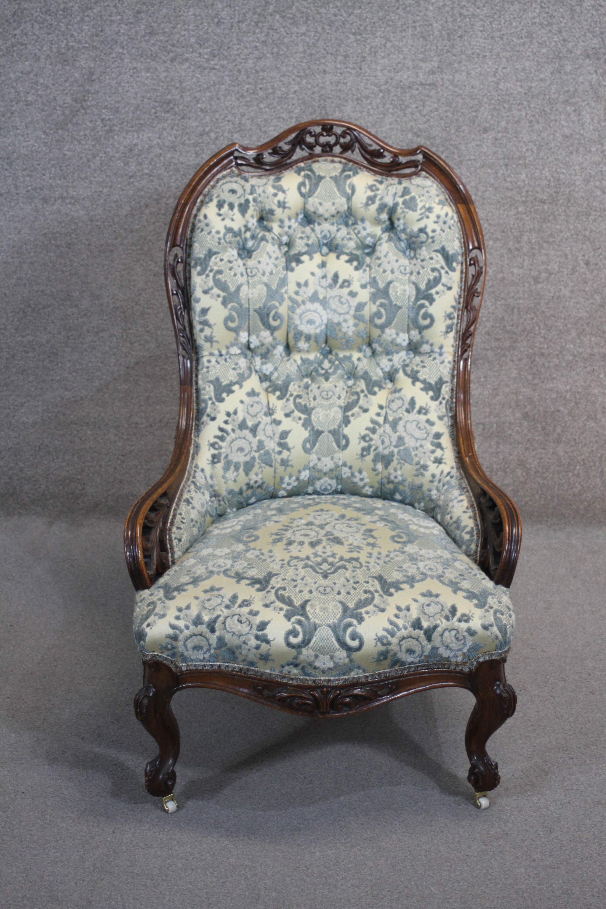 A Victorian rosewood carved frame nursing chair in buttoned upholstery on cabriole supports.