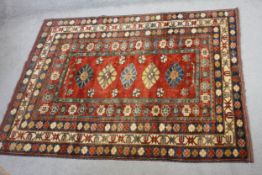 A fine hand woven Chechen rug with repeating floral motifs on a burgundy ground in wide stylised