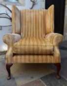A Georgian style wing back armchair in striped and piped velour upholstery on cabriole supports. H.