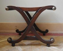 A 19th century style mahogany X frame stool with caned seat and gilt roundels resting on bun feet.