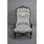 A Victorian rosewood carved frame nursing chair in buttoned upholstery on cabriole supports.