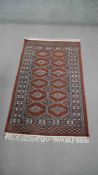 A Bokhara rug with repeating hooked lozenge medallions on a terracotta ground. L.136 W.80cm