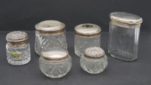 A collection of six silver 20th century topped cut glass lidded pots. Various British hallmarks.