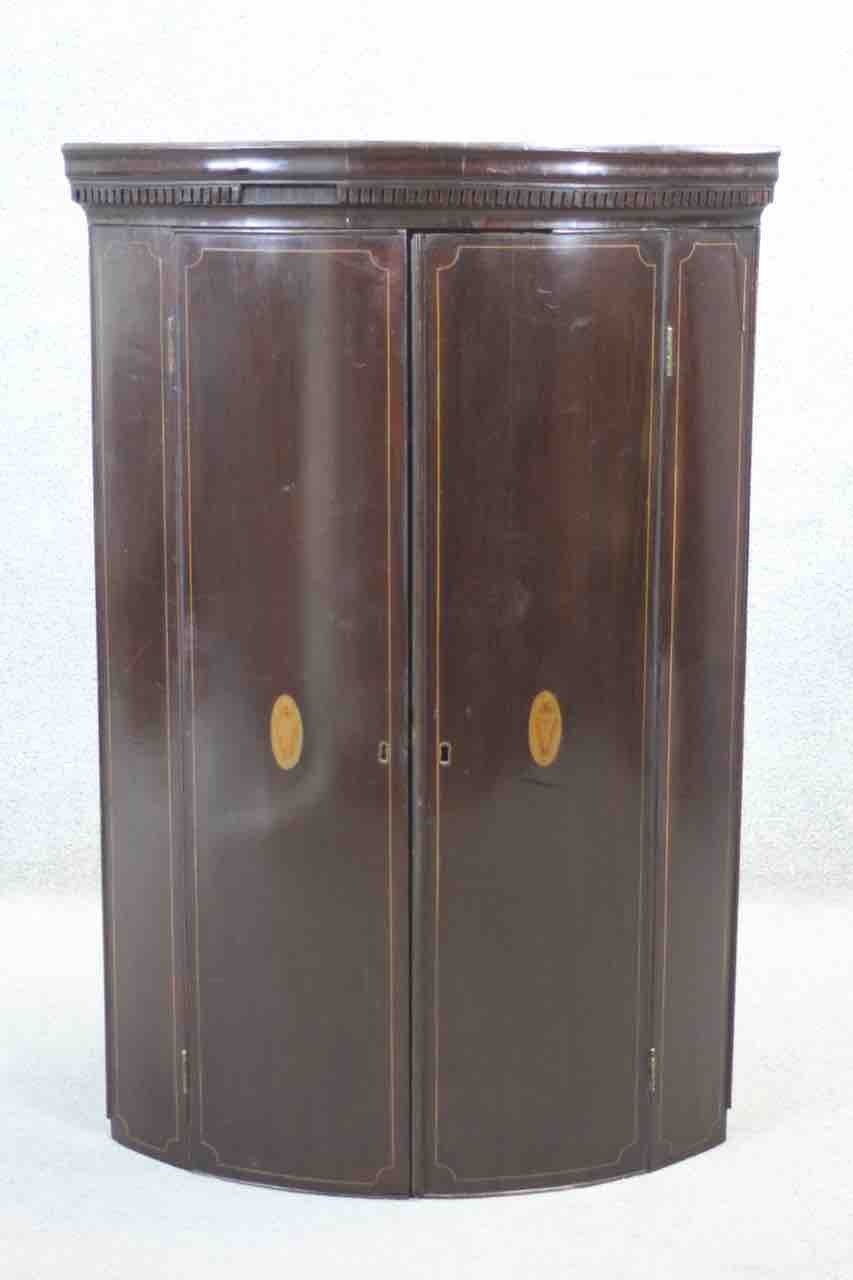 A Georgian mahogany bow fronted hanging corner cabinet with inset inlaid decoration. H.65 x W.56 x