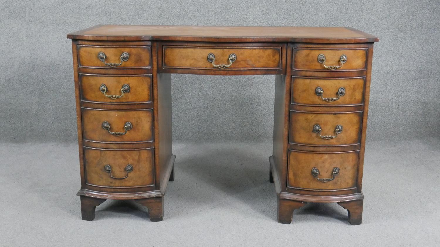 A Reprodux Georgian style figured mahogany pedestal desk with inset leather shaped top on shaped