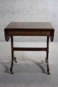 A small Regency style mahogany and ebony strung sofa table on swept supports resting on brass cup