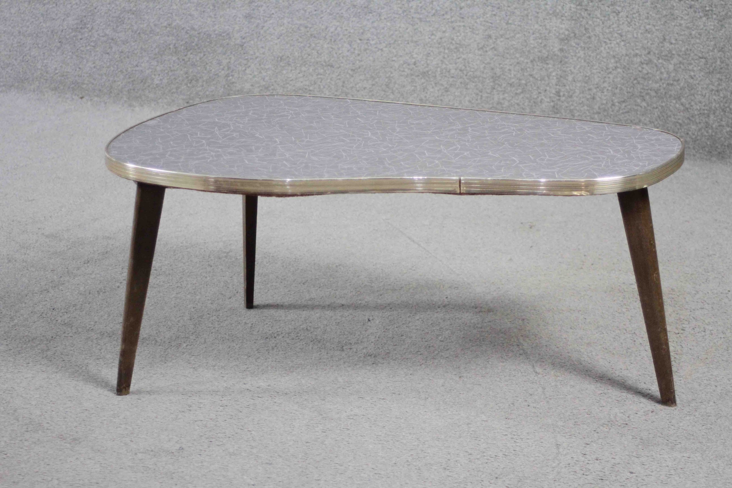 A mid century shaped coffee table with composite laminated top on splay supports. H.34 W.76 D.43