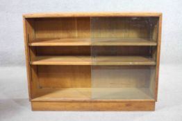 A mid century oak dwarf bookcase with sliding plate glass doors enclosing adjustable shelves on