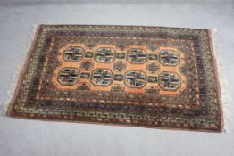 An Afghan rug with repeating medallions on a terracotta ground within stylised multiple borders. L.
