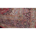 A large Keshan carpet with central floral pendant medallion on a madder field within foliate
