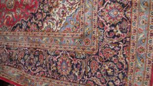 A large Keshan carpet with central floral pendant medallion on a madder field within foliate