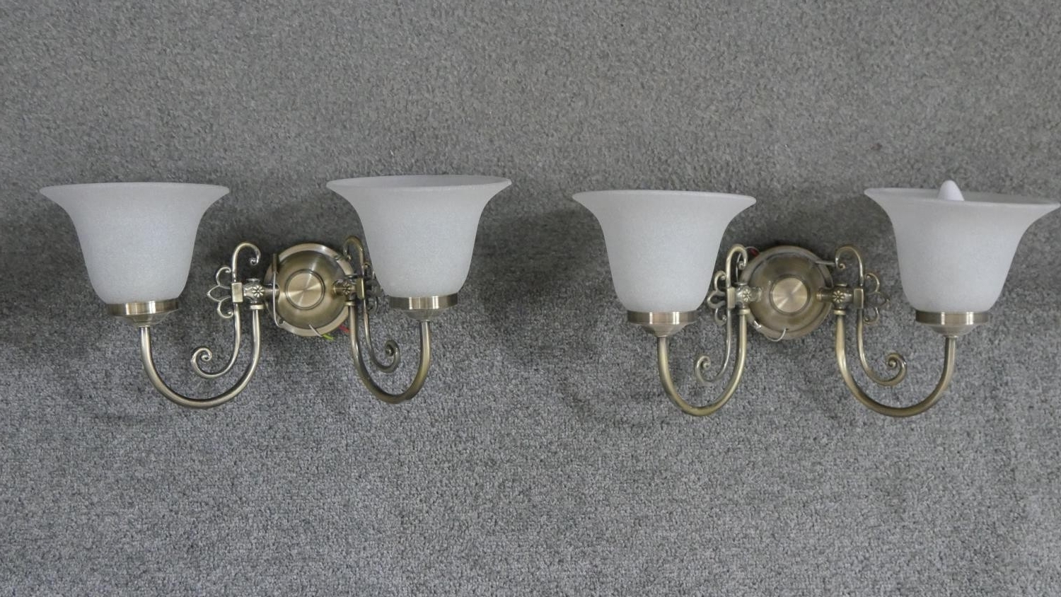 A pair of brushed brass and glass two branch wall lights. Each with two bell shaped frosted milk