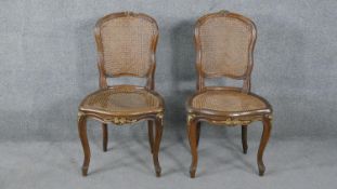 A pair of French style walnut salon chairs with carved and gilded decoration on cabriole supports.