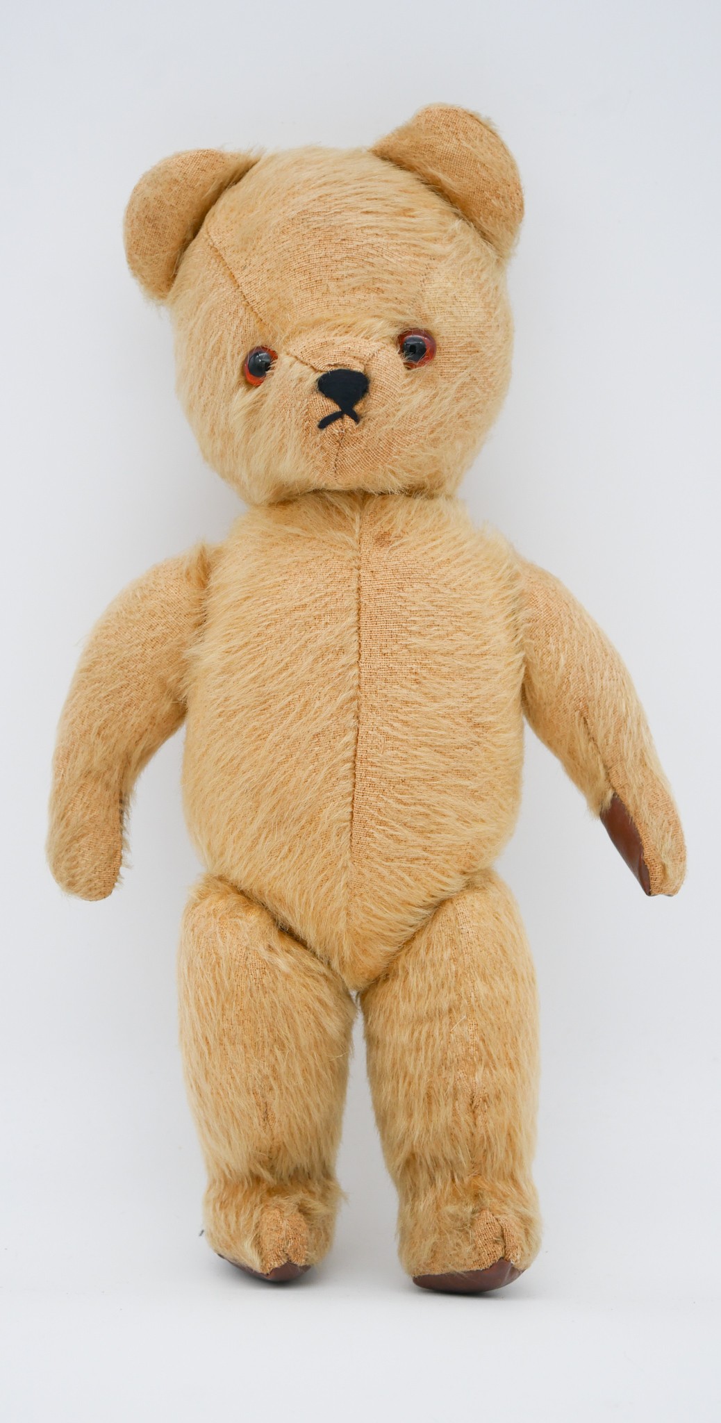 An antique yellow growler teddy bear with glass eyes and leather pads.