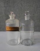 Two 19th century apothecary clear glass bottles with stoppers. One with a hand written label 'Ess