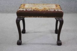 A Georgian style mahogany stool in tapestry upholstery on carved cabriole ball and claw supports.