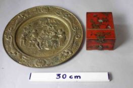 A repousse brass decorative plate with tavern scene and horn of plenty motifs along with a red