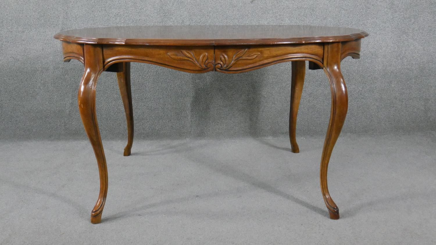 A French Provincial style walnut extending dining table with quarter veneered top and extra leaf