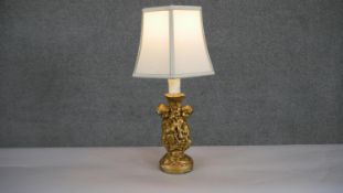 A gilded plaster cherub design table lamp with cream hexagonal shade. H.47 W.26cm