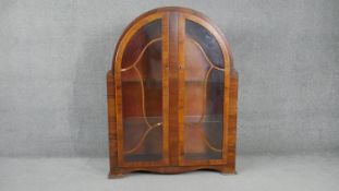 An Art Deco figured walnut display cabinet with twin arched astragal glazed doors on shaped