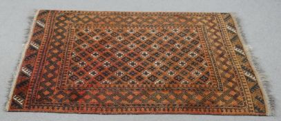 An Afghan rug with repeating stylised geometric motifs on a terracotta ground within multiple