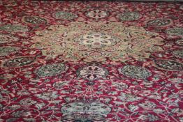 A large Wilton carpet with repeating floral medallions and trailing foliate decoration on a burgundy