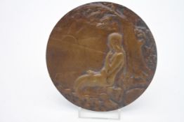 An Art Nouveau style bronze relief plaque depicting a mermaid on a rock under a tree gazing at a