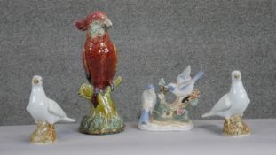 A collection of four hand painted porcelain bird figures. A majolica scarlet and blue parrot on