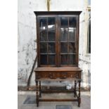 A mid century oak Jacobean style bookcase with panel glazed doors enclosing shelves above frieze