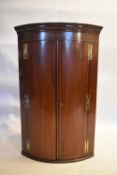 A Georgian mahogany bow fronted hanging corner cabinet with original brass work. H.118 W.74 D.48cm