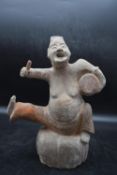 A Han or later Chinese terracotta glazed theatrical figure, perched on a stone and playing the drum.