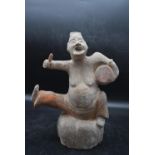 A Han or later Chinese terracotta glazed theatrical figure, perched on a stone and playing the drum.