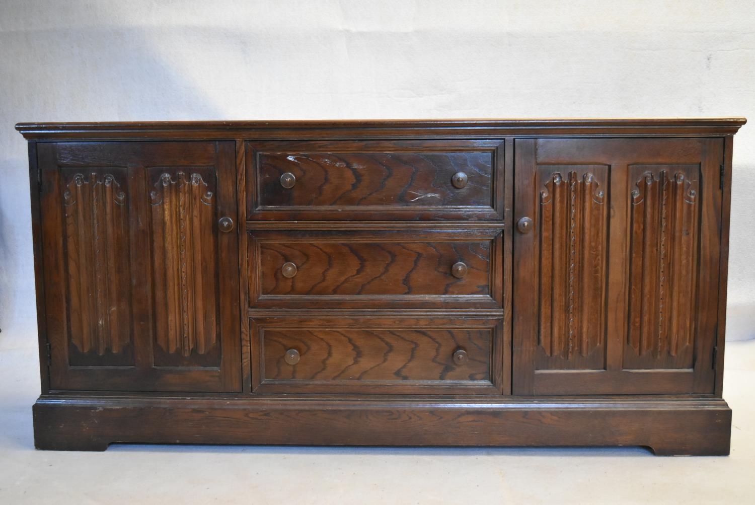 A mid century country antique style oak sideboard with a central bank of drawers flanked by linen