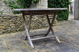 A weathered teak garden table with slatted top on X frame supports. H.75 W.121 D.121cm