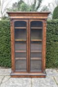 A mid Victorian rosewood and ebonised library bookcase with arched glazed doors enclosing