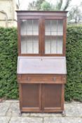 A mid century oak bureau bookcase with upper leaded glazed section above fitted interior with