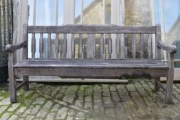 A weathered teak three seater garden bench with carved back rail and slatted back and seat on square