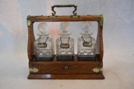 A Victorian oak three bottle tantalus with three cut crystal decanters and labels with silver