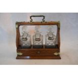 A Victorian oak three bottle tantalus with three cut crystal decanters and labels with silver