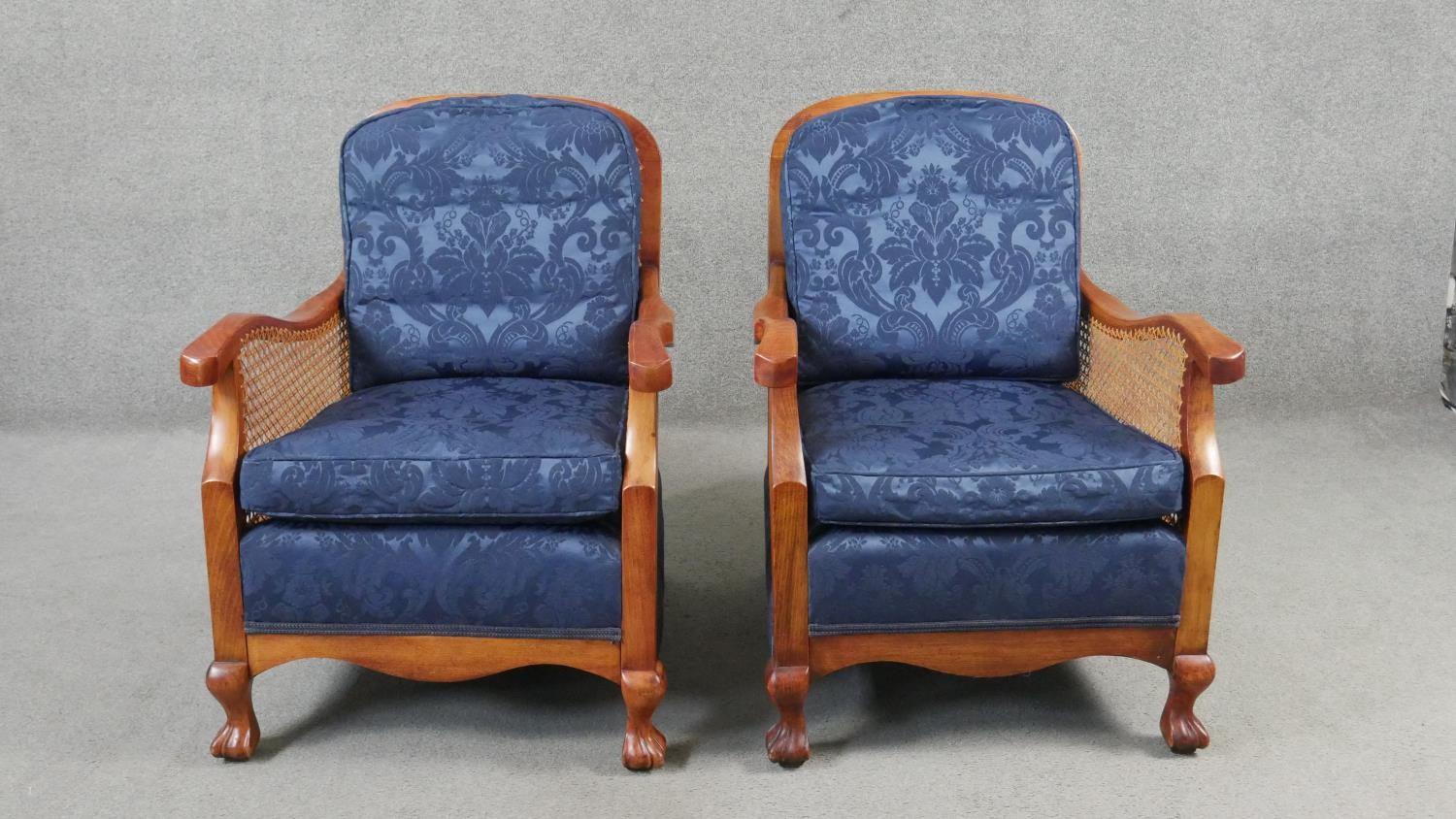 A pair of mid century vintage beech bergere armchairs with caned backs and sides on carved