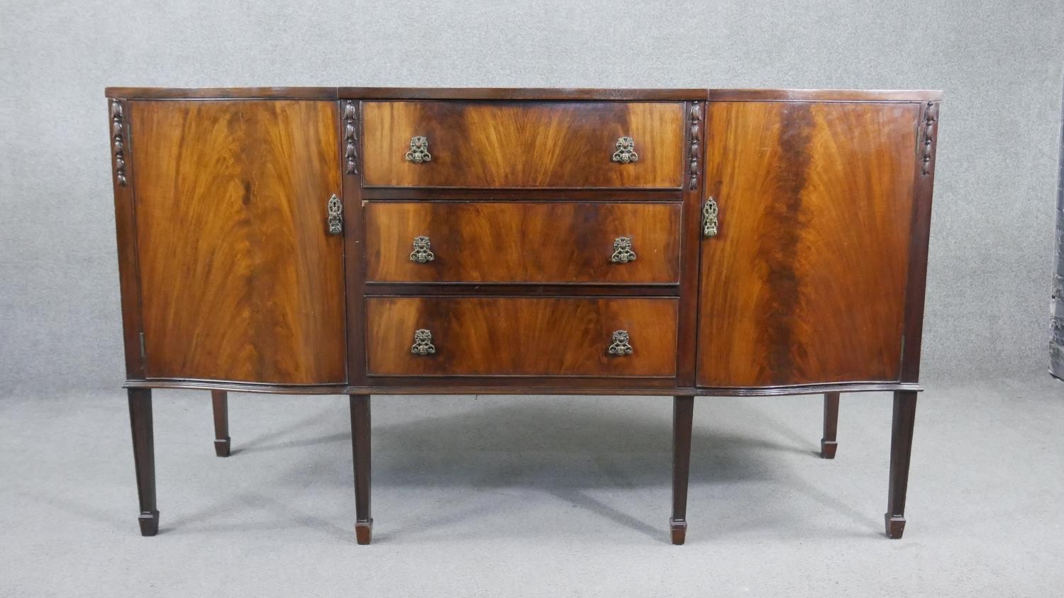 A Georgian style flame mahogany sideboard with husk carved decoration on square tapering supports.