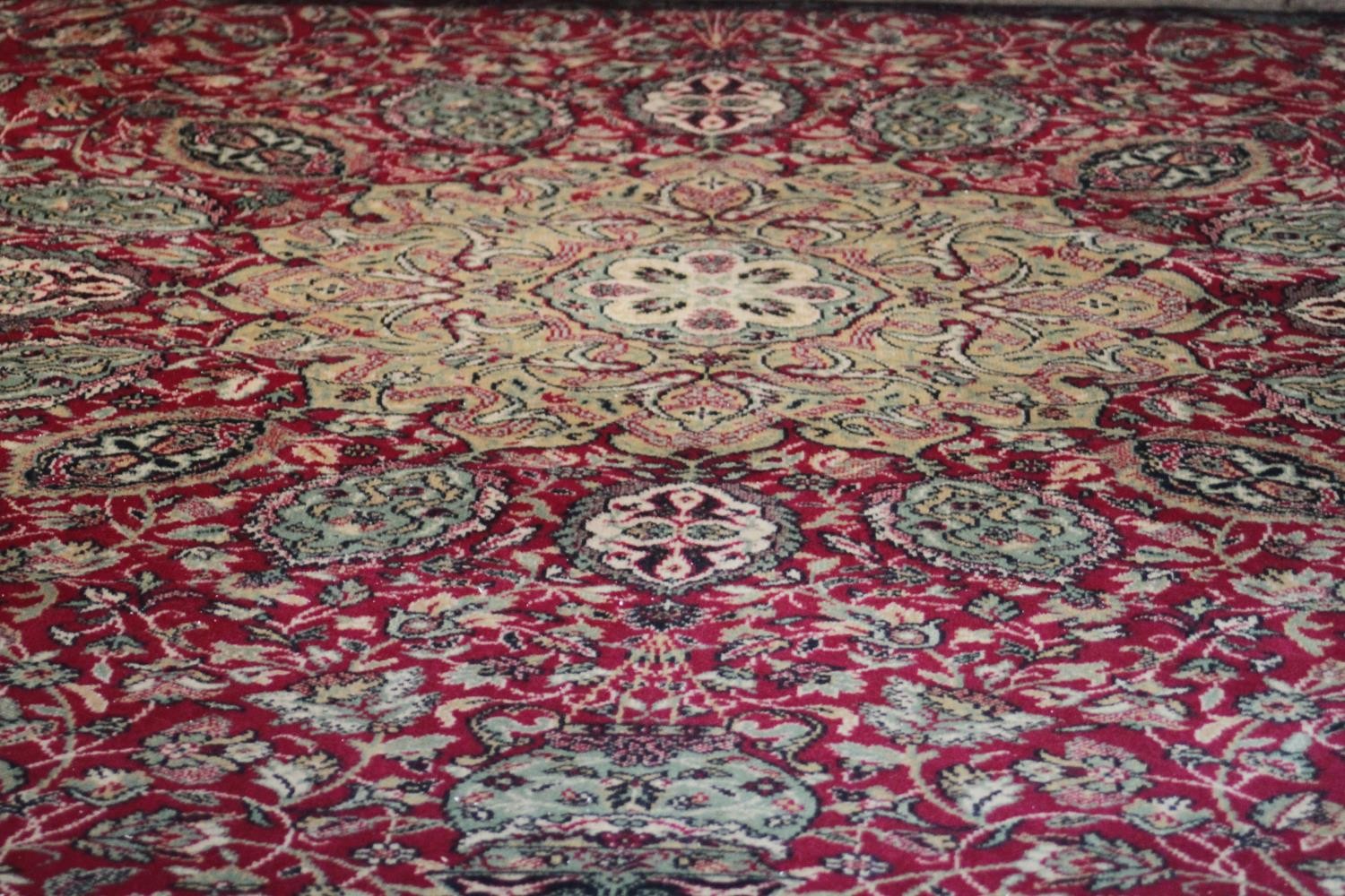 A large Wilton carpet with repeating floral medallions and trailing foliate decoration on a burgundy