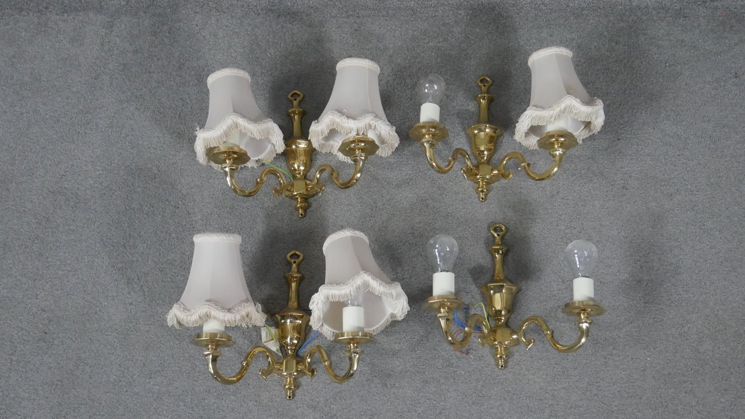 A set of four brass two branch scrolling design wall lights with cream silk shades and tassel