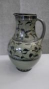 A large art pottery glazed jug with hand painted foliate design. Signed and dated to the base. H.