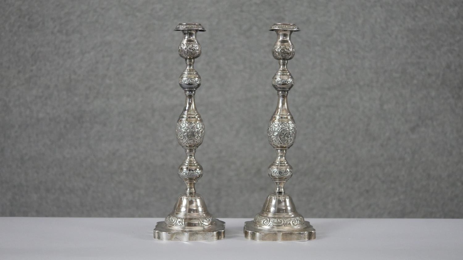 A pair of 1920'a repousse silver candlesticks with scrolling foliate design on scalloped bases.