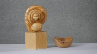 A carved pine surrealist sculpture of a snake with babys head and egg on a wooden cube plinth.