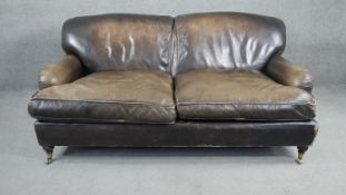 A Howard style two seater sofa in leather upholstery on turned supports terminating in brass