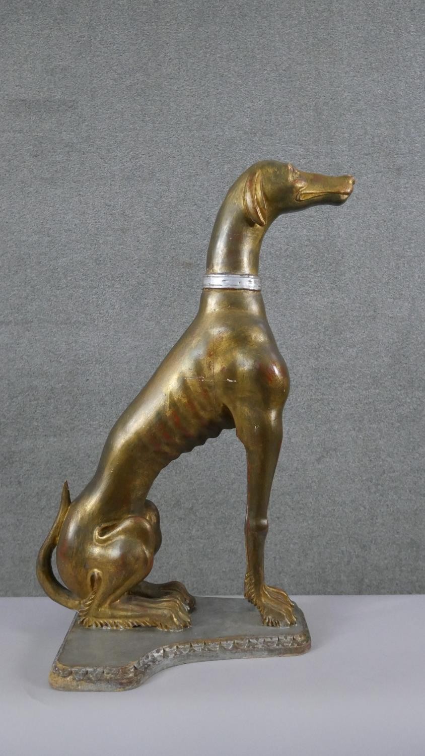 A life size early 20th century carved giltwood greyhound with collar, mounted on a wooden plinth